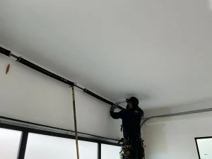 A technician reaching up to adjust a high-tension torsion spring bar during Garage Door Spring Repair.