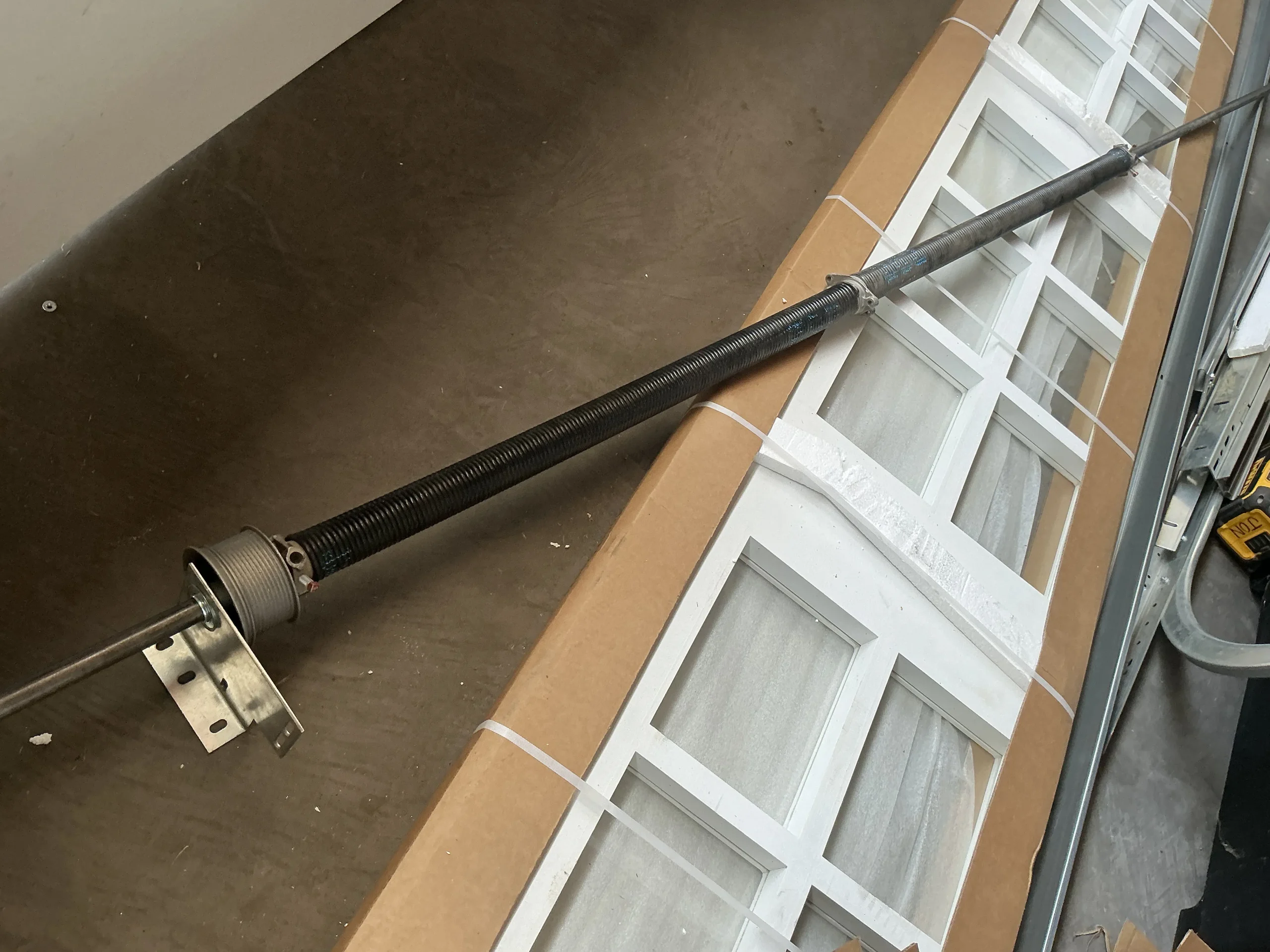 A long black metal torsion spring assembly mounted on a central shaft resting beside garage door components, illustrating Garage Door Springs.