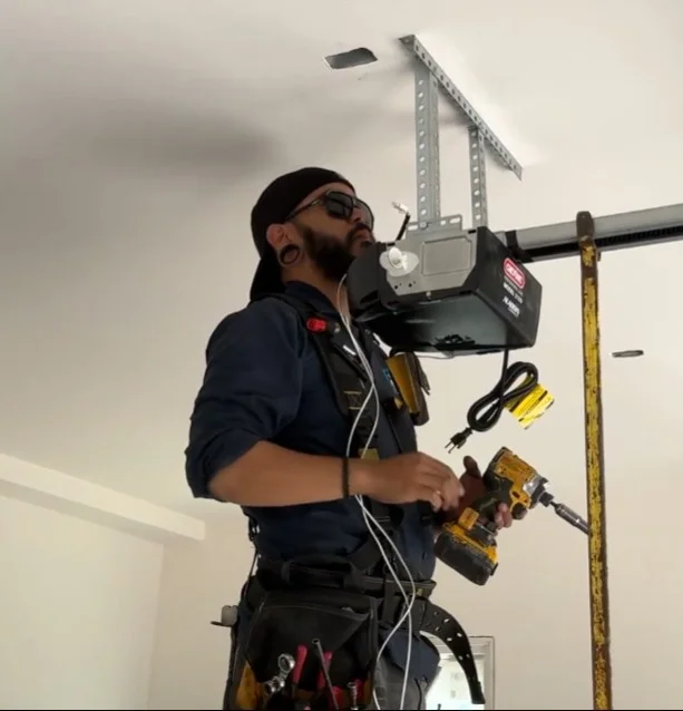 A technician holding a power drill while securing a ceiling-mounted Garage Door Opener.