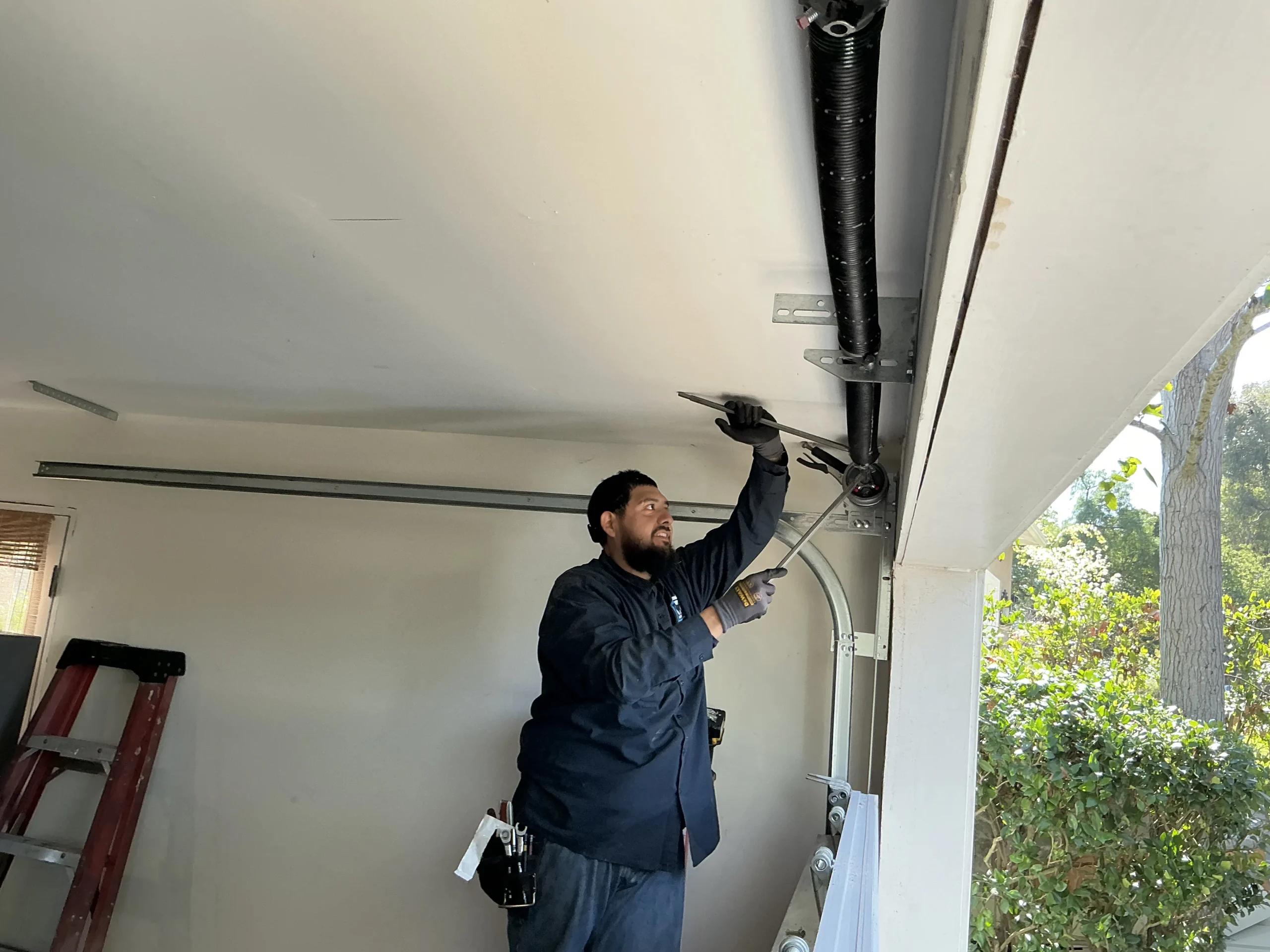A technician using winding bars to repair high-tension overhead coil components, addressing Garage Door Spring Problems.