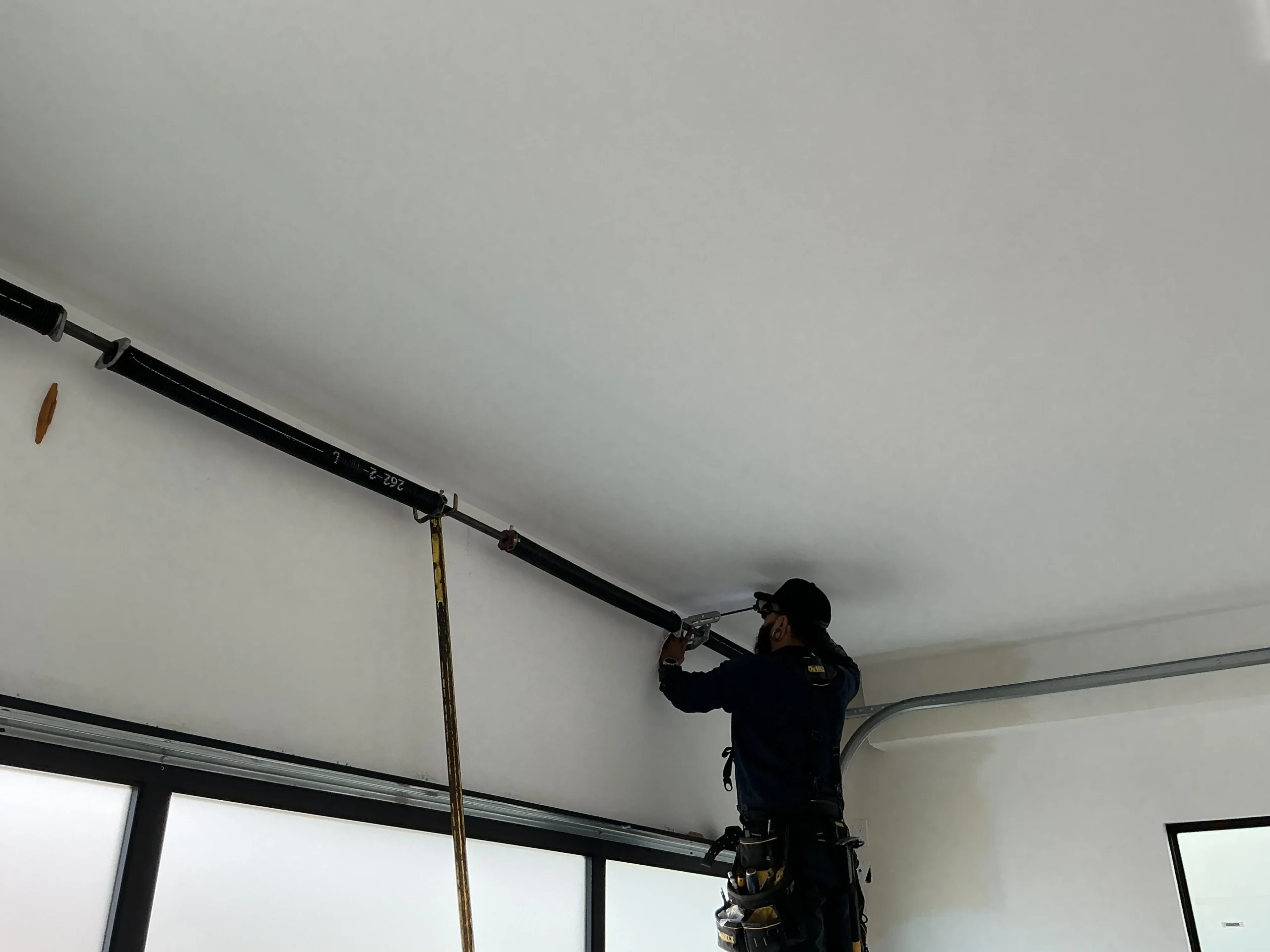 A technician working overhead to adjust a torsion spring bar system during Garage Door Spring Repair.